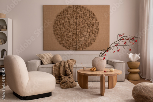 Creative composition of living room interior with mock up poster frame, beige sofa, wooden coffee table, rounded shapes armchair, vase with rowanberry and personal accessories. Home decor. Template.. © FollowTheFlow