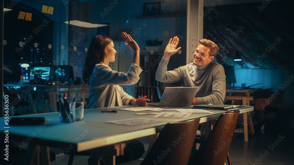 Successful Young Small Business Owners Communicating at a Meeting in Office at Night. Beautiful Female and Handsome Male Discussing Corporate Agenda and Opportunities. Managers High Five Each Other. - obrazy, fototapety, plakaty 