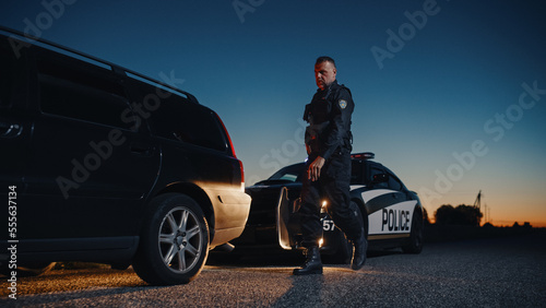 Fotografiet Portrait of Middle Aged Caucasian Cop Stepping out of a Police Car and Approaching a Pulled Over Car with Caution