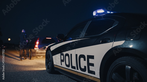 Portrait of Middle Aged Caucasian Cop Approaching a Pulled Over Vehicle with Caution. Drunk Driver Being Stopped by an Officer to Inspect his Papers. Camera Focus on Police Car