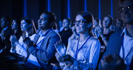 Young Woman Sitting in a Crowded Audience at a Business Conference. Female Attendee Cheering and Clapping After a Motivational Keynote Speech. Auditorium with Young Successful Businesspeople.