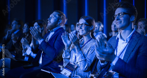 Young Female Sitting in a Crowded Audience at a Science Conference. Delegate Cheering and Applauding After an Inspirational Keynote Speech. Auditorium with Young Successful Specialist. photo