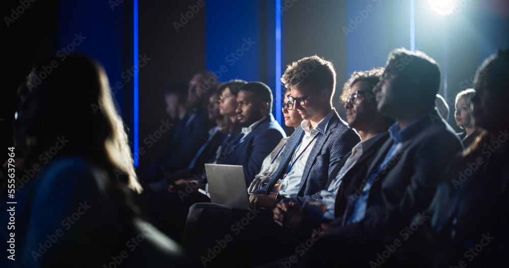 Obraz premium Male Sitting in a Dark Crowded Auditorium at a Tech Conference. Professional Using Laptop Computer. Specialist Watching Innovative Technology Presentation About New Hardware and High Tech Solutions.