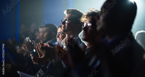 Young Man Sitting in a Crowded Audience at a Business Conference. Male Attendee Cheering and Clapping After a Motivational Keynote Speech. Auditorium with Young Successful Businesspeople.