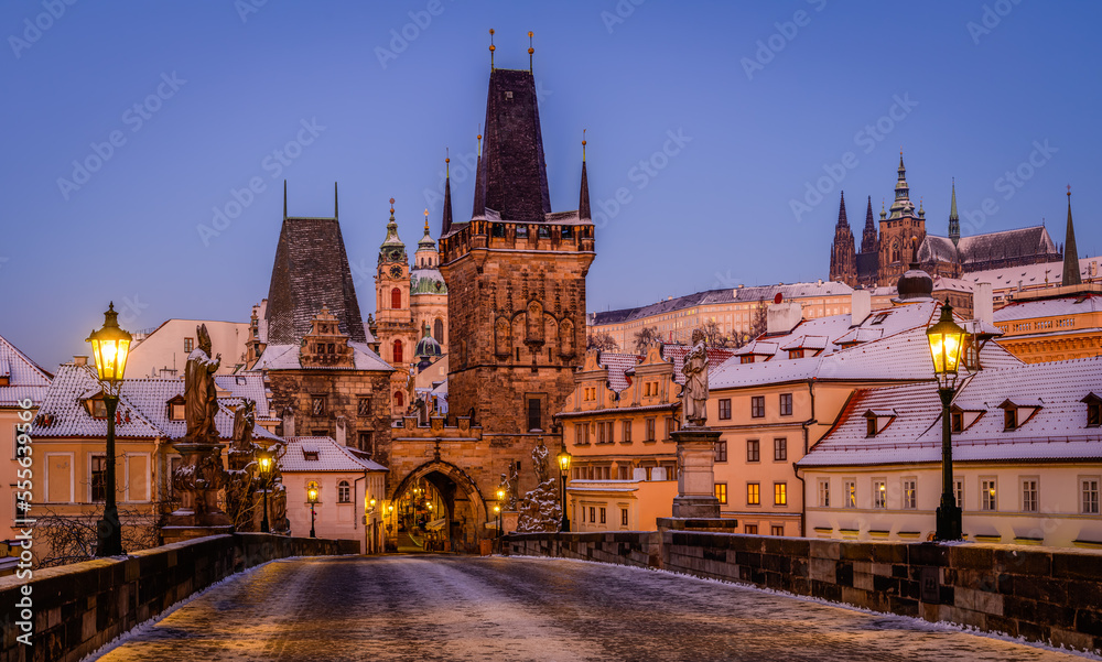 Charles Bridge covered in snow with shining lanterns in Prague during blue hour in the winter morning.