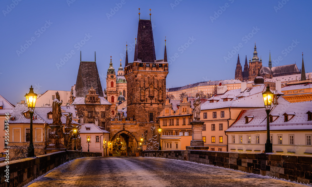 Fototapeta premium Charles Bridge covered in snow with shining lanterns in Prague during blue hour in the winter morning.
