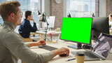 Portrait of Young Caucasian Man Working on Laptop and Green Screen Computer During Day in Modern Bright Office. Creative Software Developer Using Chroma Key Display PC