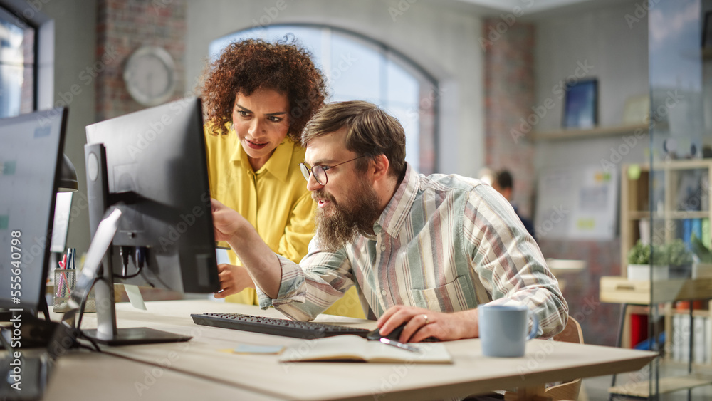 Portrait of Two Creative Colleagues Collaborating and Pointing at the Computer Screen in Modern Bright Office. Biracial Young Woman Discussing Work with Caucasian Male Assistant. Portrait of Two Creative Colleagues Collaborating and Pointing at the Computer Screen in Modern Bright Office. Biracial Young Woman Discussing Work with Caucasian Male Assistant.