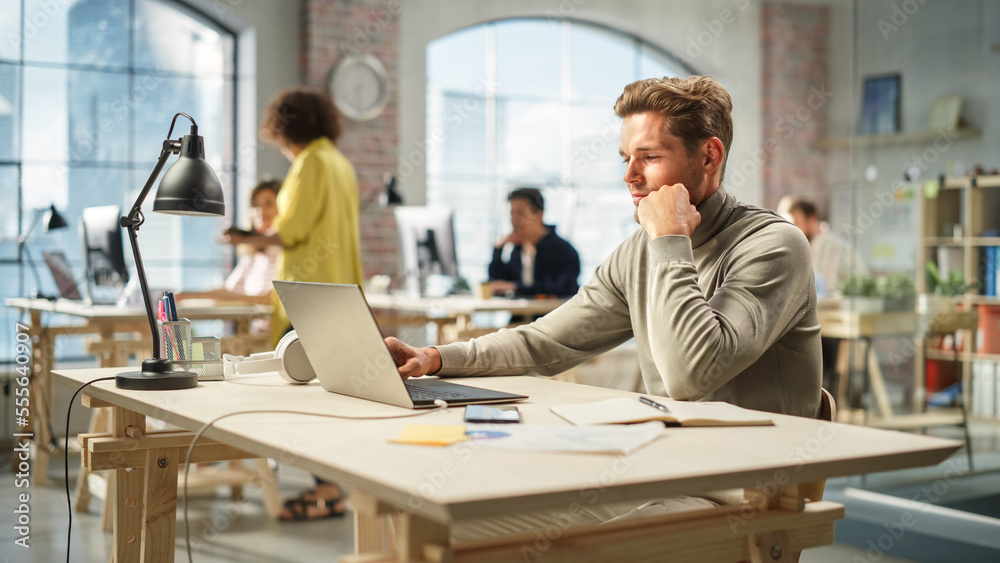 Portrait of Caucasian Productive Young Man Working on Laptop in an Active Office. White Businessman Developing an E-commerce Strategy. Busy Colleagues Working in the Background.