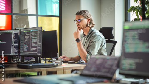 Focused Caucasian Man Coding On Desktop Computer in Stylish Office Space. Male Software Engineer Developing Innovative Application For Business Customers in Technological Start-up Company.