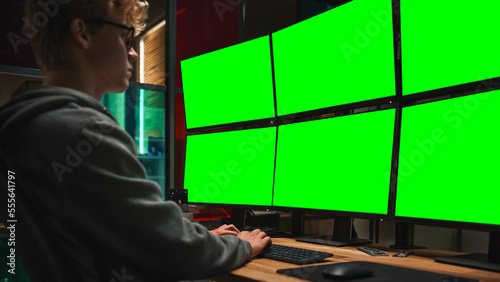 Young Caucasian Man Writing Code on Professional Six Monitors Setup With Green Screen Chromakey. Male Cyber Security Expert Controlling Data Protection System in International Intelligence Agency.