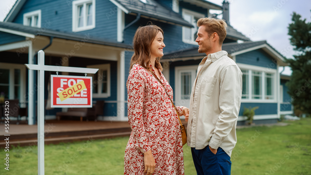 Portrait of a Beautiful Young Couple in Love Standing in Front Their New Home. Successful Homeowners Looking at Camera and Smile. Female in a Dress Expecting a Baby. Real Estate Housing Market Concept Portrait of a Beautiful Young Couple in Love Standing in Front Their New Home. Successful Homeowners Looking at Camera and Smile. Female in a Dress Expecting a Baby. Real Estate Housing Market Concept