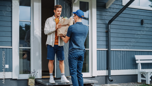 Portrait of a Young Man Working in a Grocery Delivery Service, Bringing a Bag Full of Fresh Vegetables and Other Food Items to a Residential Area Home. Addressee Opens Signs a Waiver on Tablet.