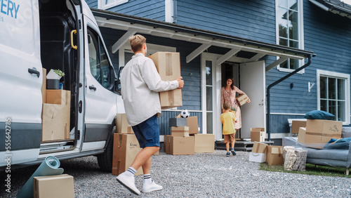Handsome Man Unloading a Cargo Van Full of Cardboard Moving Boxes. Young Happy Family with a Son Moving to Their Dream Home in the Suburbs. Delivery Transportation Car Sharing Service.