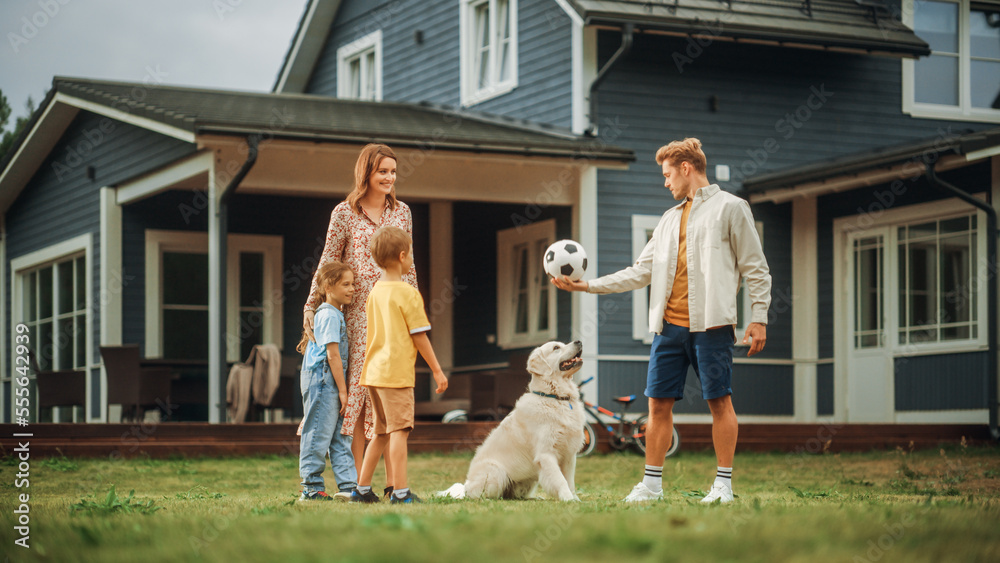 Happy Young Couple with Kids, Playing Football with a Sporty White Golden Retriever. Cheerful People Playing Ball with Pet Dog on a Lawn in Their Front Yard in Front of the House.