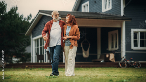 Portrait of a Healthy Senior Couple Walking Outdoors Their Residential Area Home, Embracing Each Other. Loving Adults, Talk, Have Fun, Point to the Distance and Enjoy Their Happy Retirement Life.