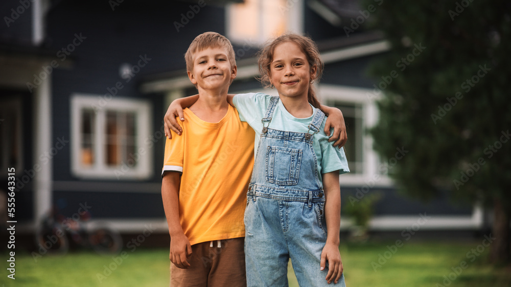 Young Happy Brother and Sister Standing in Front of a Country House, Embracing Each Other, Looking at Camera and Smiling. Two Kids Enjoying Childhood and Friendship.