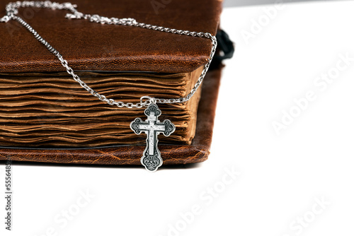 isolated on a white background jewelry silver cross on a chain with a shadow lies on an old book