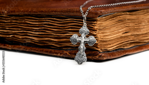 isolated on a white background jewelry silver cross on a chain with a shadow lies on an old book