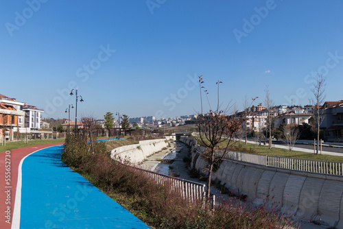 walking and cycling path sunny weather wooden structures and waterway blue and red roads street lighting trees and houses on the hill