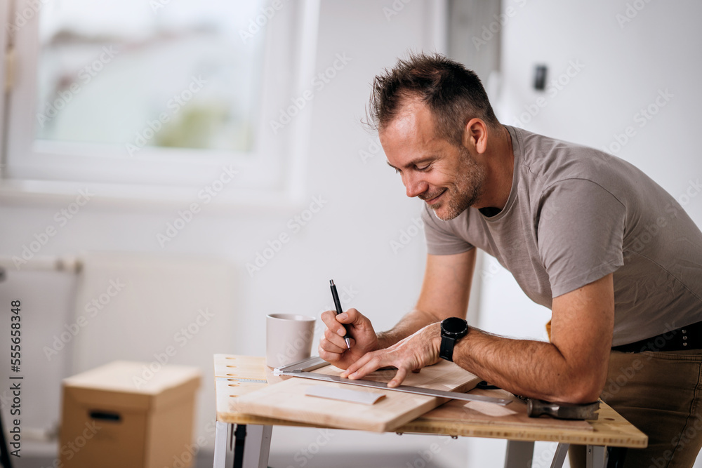 A handsome smiling carpenter measuring a wooden board