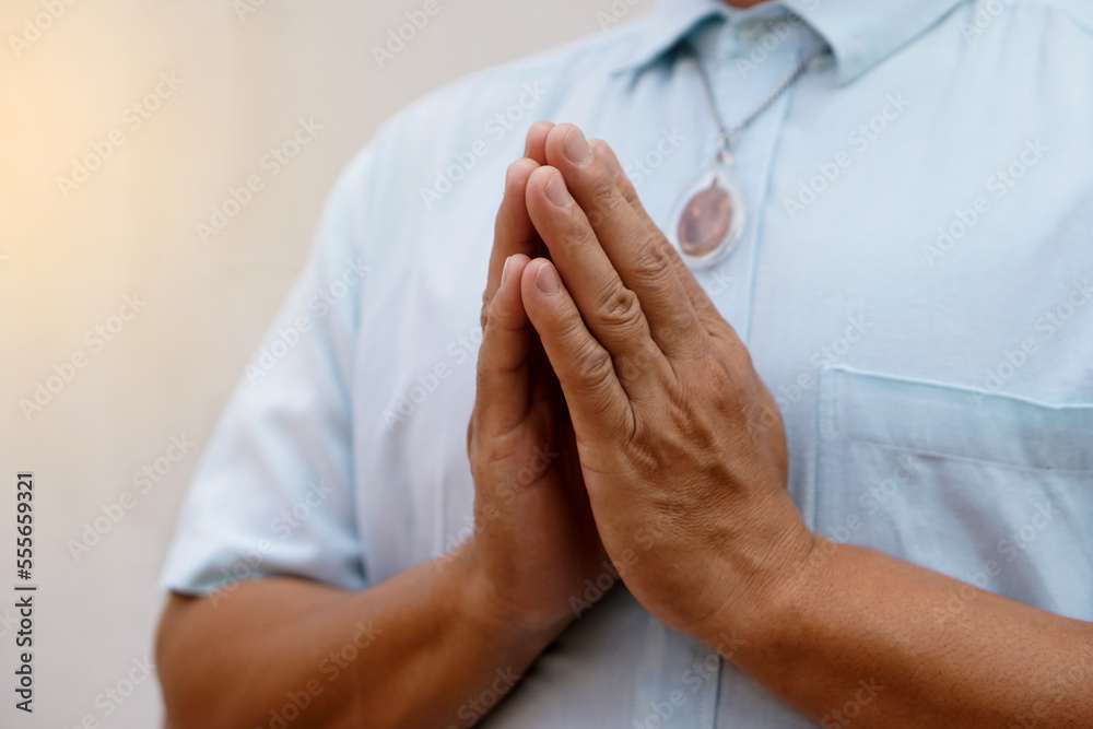 Closeup man in blue shirt ,wears Buddha amulet, praying with hands buddhist pray gesture, Wai in Thai culture. Concept, woreship for lucky, faith and belief. Pattern of respect and greeting.          