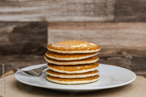 A large plate stack of pancakes with a fork against a wood background plain with no syrup