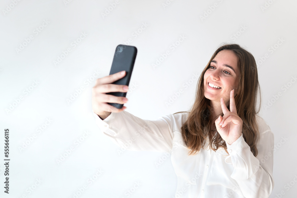 Young woman taking a photo or selfie with her mobile phone on a grey background.