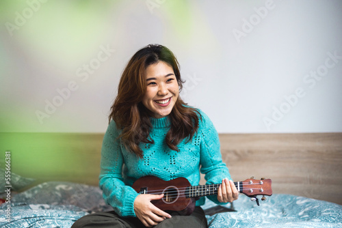 Young woman having fun playing Ukulele in her studio apartment 