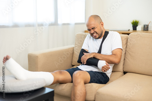 Man suffered pain from accident fracture broken bone injury with leg splints in cast neck splints collar arm splints sling support arm in living room. Social security and health insurance concept. © Chanakon