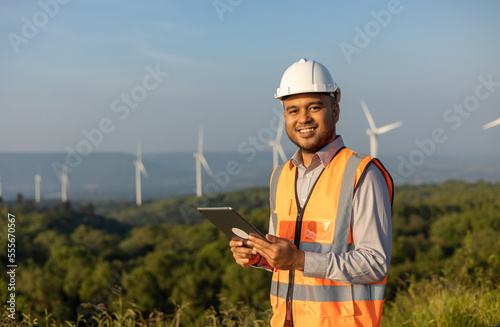 Engineer India man working with tablet at windmill farm Generating electricity clean energy. Wind turbine farm generator by alternative green energy. Asian engineer checking control electric power © Chanakon