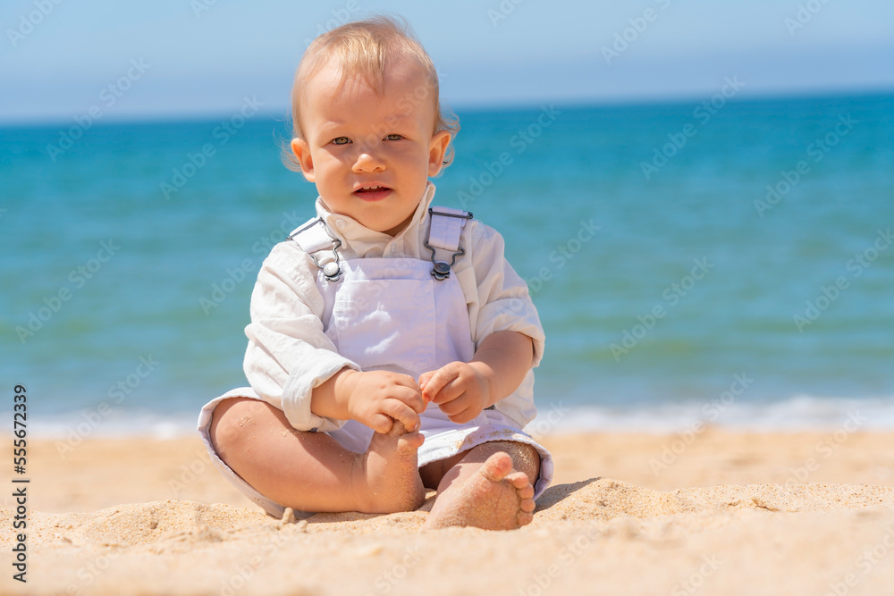 Little cheerful boy child sits on the sand on the beach. Sunny day. Little cheerful boy child sits on the sand on the beach. Sunny day.