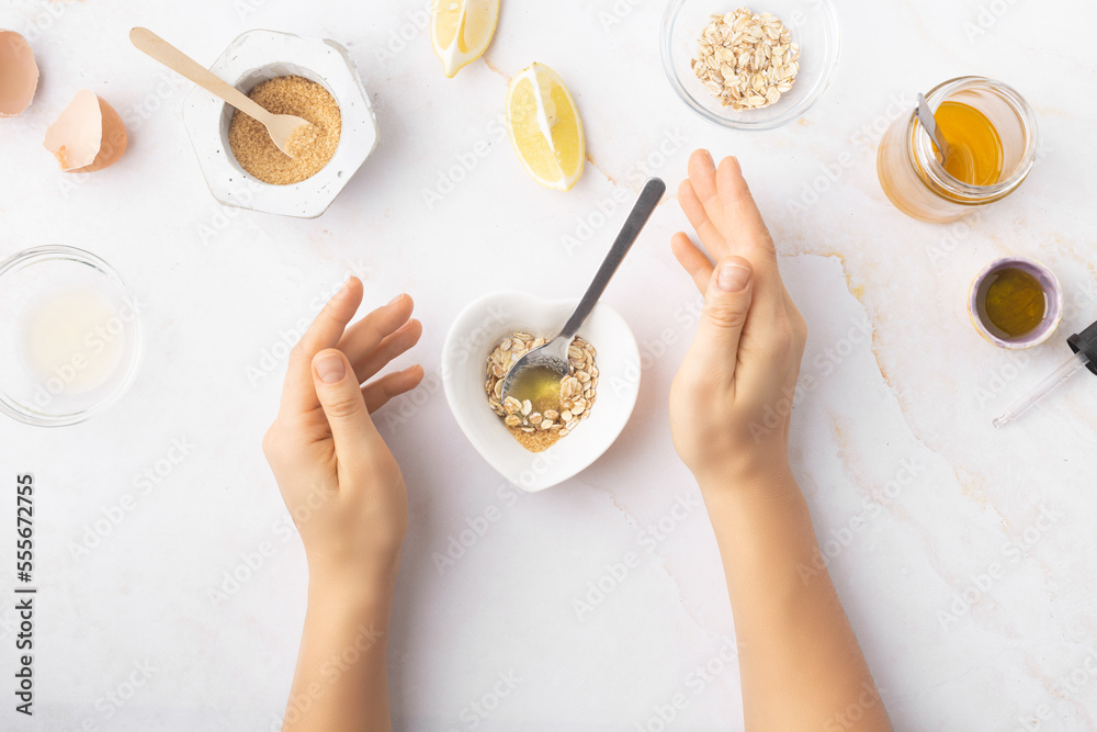 Flatlay with homemade beauty products: fresh ingredients like oat, honey, lemon, banana, egg, olive oil. Female hand holding a jar of cream. Overhead view, copy space. Flatlay with homemade beauty products: fresh ingredients like oat, honey, lemon, banana, egg, olive oil. Female hand holding a jar of cream. Overhead view, copy space.