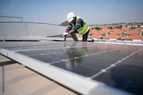 African American engineer man use electric screwdriver working with solar panel on roof factory