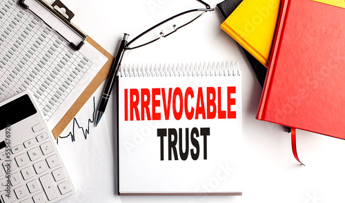 IRREVOCABLE TRUST text on notebook with clipboard and calculator on white background photo