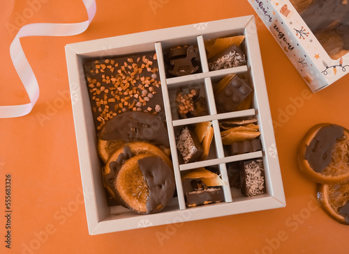 Chocolate candies in a red craft box wooden Christmas background fir branches of a New Year's toy. Flat layout top view.  Chocolate mediants, bites, candies in a gift box for Christmas and New Year ce