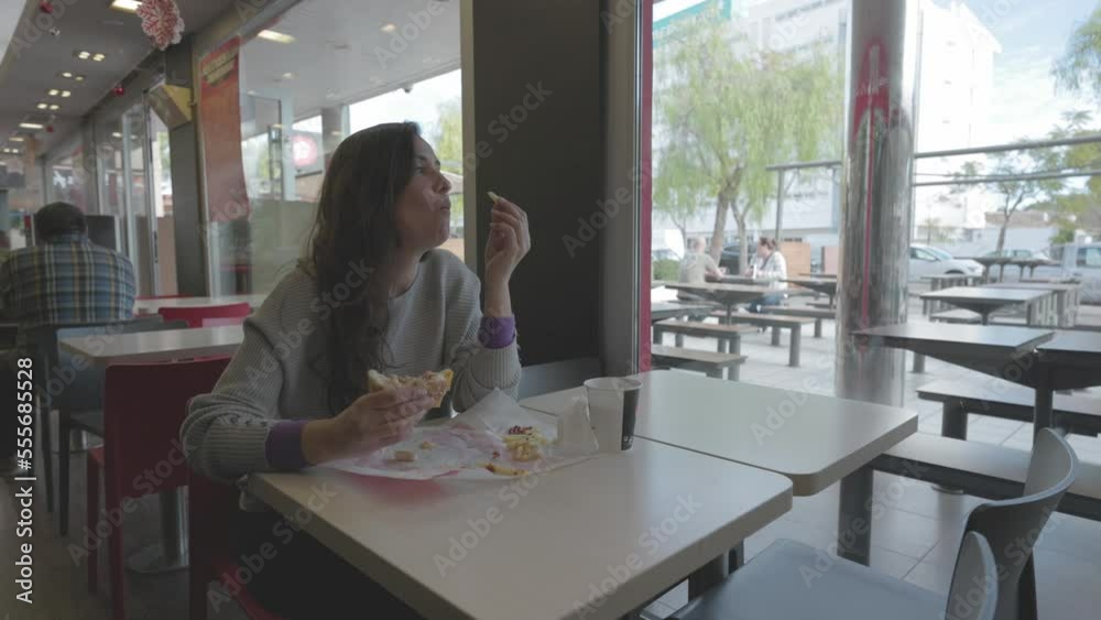 Mujer comiendo hamburguesa en restaurante comida rápida (Formato LOG para edición y corrección de color profesional)