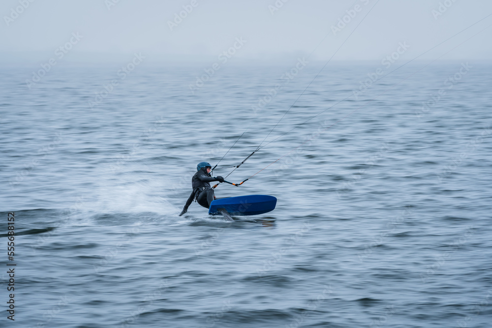 Fast Hydrofoil kitesurfer riding fast in misty winter conditions with motion blur Fast Hydrofoil kitesurfer riding fast in misty winter conditions with motion blur
