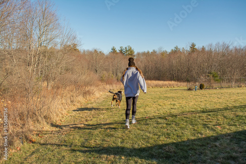 a woman running with her swiss mountain dog in the sunny cold countryside in New England, USA in winter