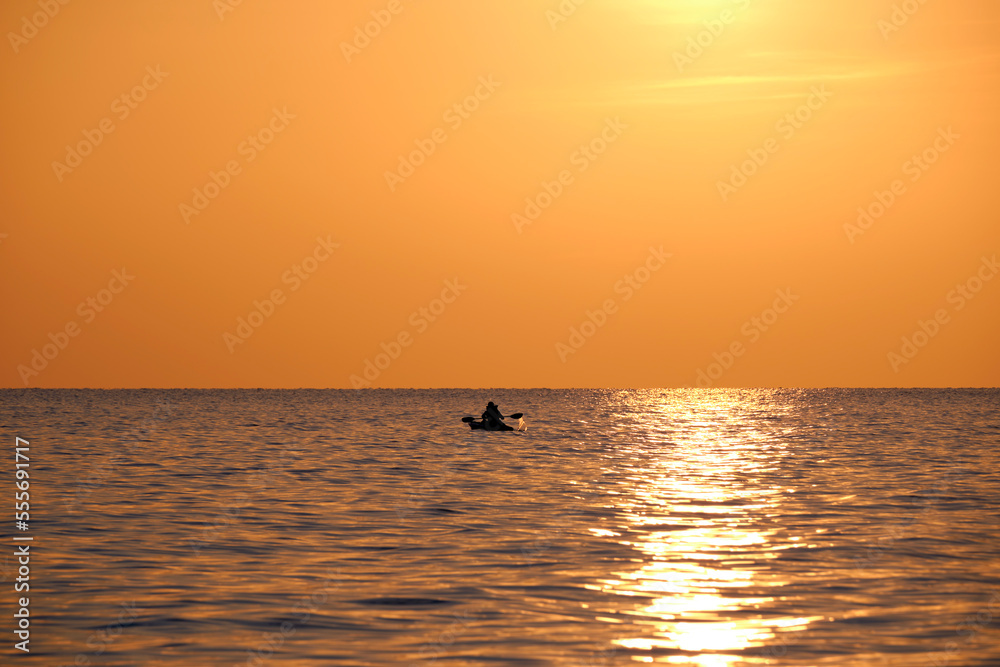 Dark figure of sportsman rowing alone on his kayak boat on sea water at sunset. Active extreme sports concept