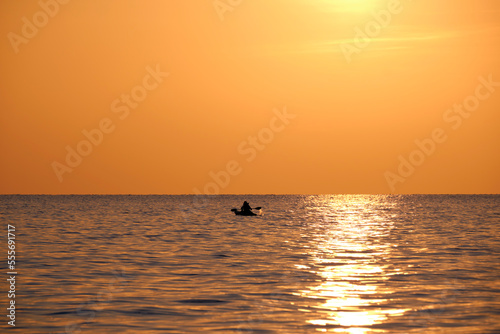 Dark figure of sportsman rowing alone on his kayak boat on sea water at sunset. Active extreme sports concept © bilanol