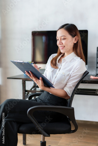 Asian businesswoman secretary sitting happily working on laptop Take notes attentively and smile happily doing the assignments.