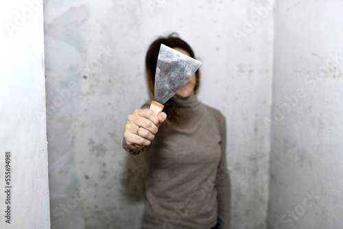 woman showing a scraper in front during renovation or painting work. concept preparing the walls for wallpapering or painting