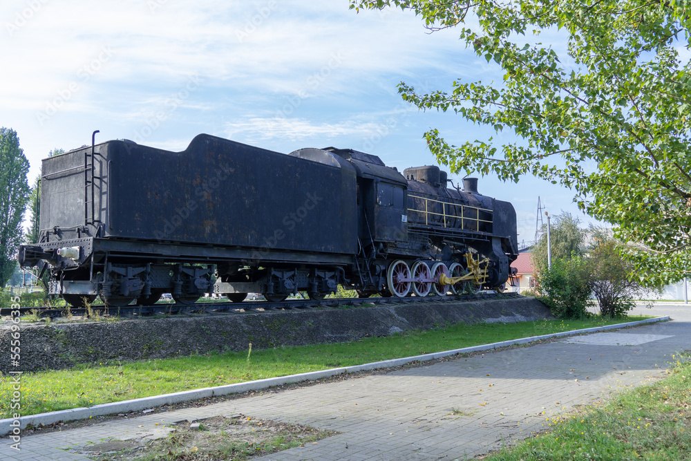 Fototapeta premium Monument old soviet locomotive. Rarity transport of communism. Steam engine train from second world war stands on pedestal in city park. Inscription says - USSR and forward on west. Dnipro Ukraine.