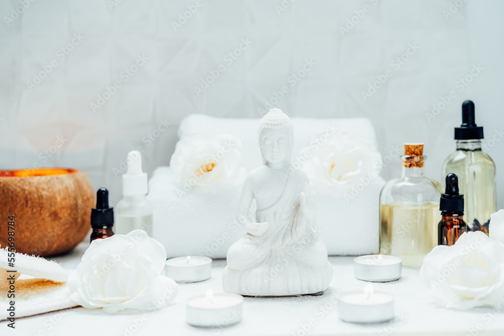 Spa and wellness massage kit and White Buddha statue. Concept of Asian relaxing spa procedure with essential oils. Alternative medicine and body care. Selective focus. copy space.
