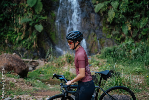 Fototapeta Naklejka Na Ścianę i Meble -  A young female cyclist is carrying her gravel bike by the waterfalls.