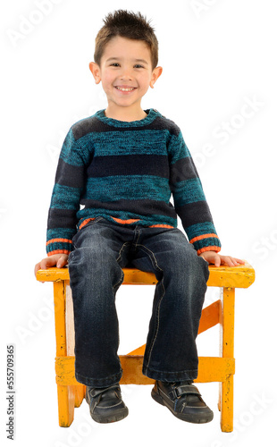Isolated boy in jeans and striped pullover smiling sitting on a yellow bench.
