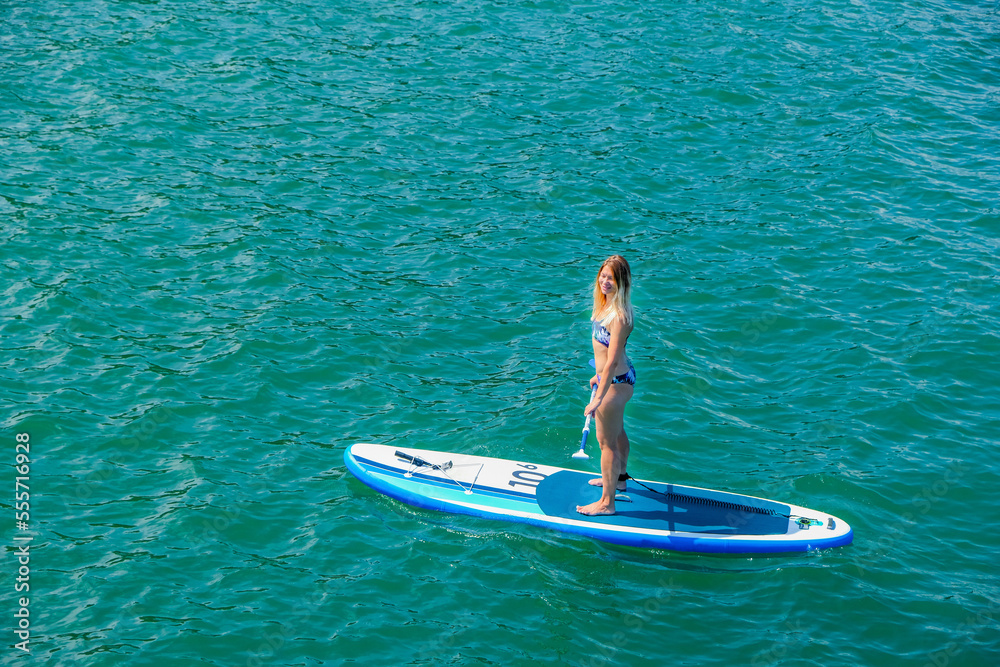 SUP Stand up paddle board. Blond girl sailing on paddle board in sea. Aerial view. Woman on summer holidays vacation lifestyle. Mtsvane Kontskhi Beach, Batumi, Georgia. SUP Stand up paddle board. Blond girl sailing on paddle board in sea. Aerial view. Woman on summer holidays vacation lifestyle. Mtsvane Kontskhi Beach, Batumi, Georgia.
