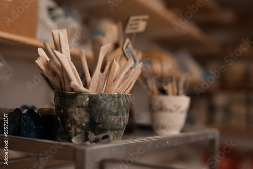 pottery, workshop, ceramics art concept - closeup on two unfired clay small cups and sculpting tools set on wooden table, clay stacks, some profiles, top view