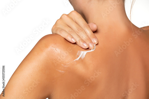 Close up young woman smearing shoulder with cream. Back view